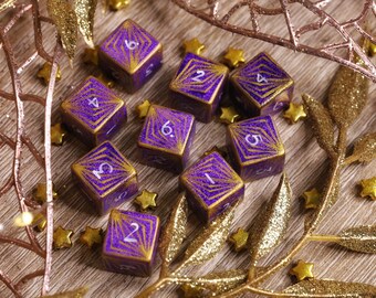 May include: Nine purple and gold dice with white numbers on each face. The dice are scattered on a wooden surface with gold glitter and a gold twig.