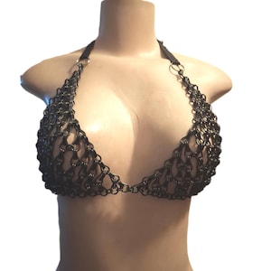 May include: A black chainmail halter top with a triangle cup design. The top is made of small, interlocking metal rings, creating a mesh-like appearance. The halter straps are black and attached to the cups with metal rings. The top is displayed on a mannequin.