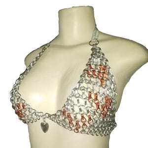 May include: Silver chainmail bikini top with copper accents and a heart-shaped charm. The halter top is displayed on a mannequin. The chainmail is woven in a triangular pattern.