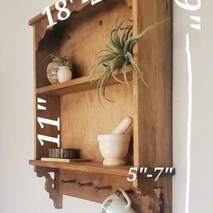 Puede incluir: Estanter&iacute;a de pared de madera, de aproximadamente 74 cm de altura, con dos estantes y una fila inferior de clavijas. El estante superior mide 46-61 cm de ancho. El estante inferior mide 13-18 cm de profundidad. Una taza cuelga de una clavija.