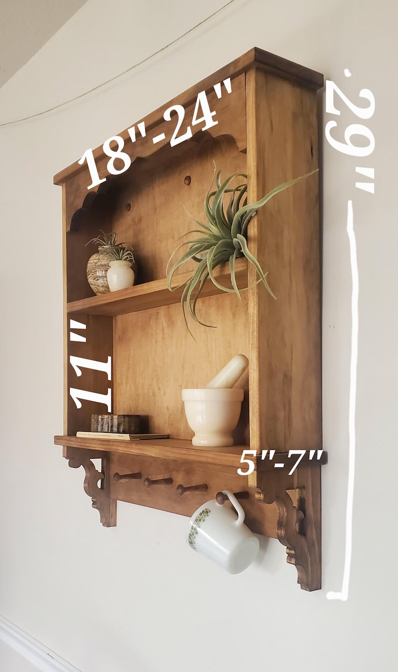 Puede incluir: Estanter&iacute;a de pared de madera, de aproximadamente 74 cm de altura, con dos estantes y una fila inferior de clavijas. El estante superior mide 46-61 cm de ancho. El estante inferior mide 13-18 cm de profundidad. Una taza cuelga de una clavija.