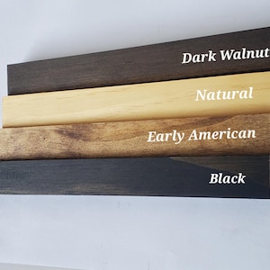 Puede incluir: Primer plano de cuatro tablas de madera, cada una te&ntilde;ida de un color diferente: nogal oscuro, natural, early american y negro. Los nombres de los colores est&aacute;n escritos en texto blanco en cada tabla.