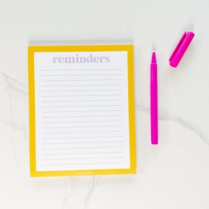 May include: Yellow notepad with the word "reminders" in purple text at the top. The notepad has lined paper and a pink pen is next to it.
