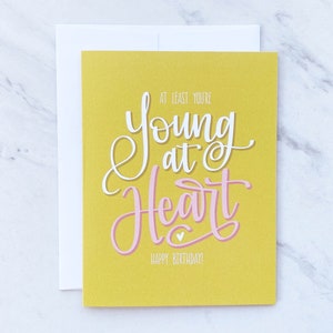 Au moins, vous avez le coeur jeune / Joyeux anniversaire / Carte de voeux / Célébration / Célébration / Lettrage manuscrit / Calligraphie / Or / Rose
