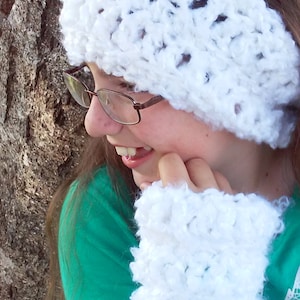 May include: A white crocheted headband with a lacy pattern. The headband is worn by a person with brown hair and glasses. The person is wearing a green shirt.