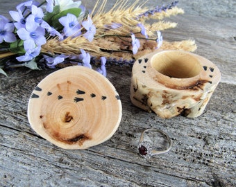 May include: A wooden ring box with a natural wood finish and black paw prints. The lid is open and a silver ring with a red gemstone is inside.