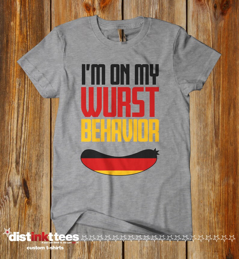Puede incluir: Una camiseta gris con el texto "I'm on my wurst behavior" en negro y un gr&aacute;fico de salchicha con los colores de la bandera alemana.