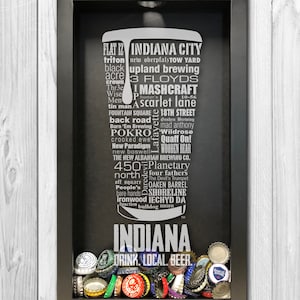 May include: A black shadow box with a white graphic of the word "Indiana" surrounded by the names of Indiana breweries. The shadow box is filled with bottle caps. The text at the bottom reads "Drink Local Beer."