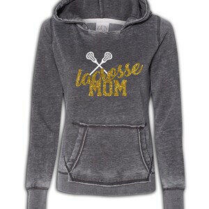 May include: A gray hooded sweatshirt with a distressed look. The front of the sweatshirt has a gold glitter design that says "lacrosse MOM" with two white lacrosse sticks crossed behind the text.