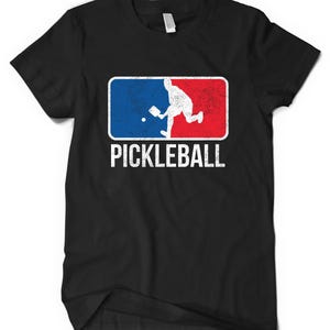 May include: Black t-shirt with a white silhouette of a person playing pickleball in a red, white, and blue logo. The text "Pickleball" is below the logo.