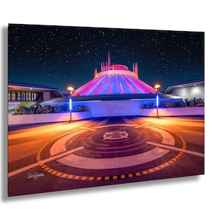 May include: A nighttime photograph of a futuristic-looking building with a conical roof illuminated in pink and blue. The foreground features a circular design with a symbol, and the sky is filled with stars. The image is a print.