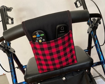May include: A black walker with a red and black plaid fabric pouch attached to the handlebars. The pouch has two pockets, one holding a remote control and the other holding a cell phone.
