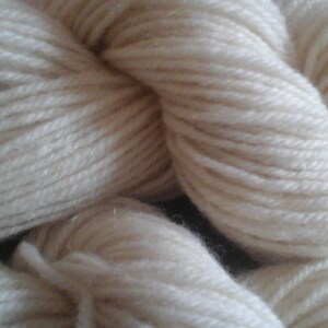 May include: Close-up of off-white yarn, tightly wound into a skein. The yarn has a soft, textured appearance, suggesting a natural fiber. Ideal for knitting, crocheting, or other fiber arts projects.