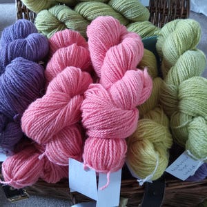 May include: A basket filled with various colours of yarn, including purple, pink, and green. The yarn is arranged in a variety of ways, some in balls, some in skeins, and some in loose strands.