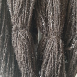 Könnte beinhalten: Nahaufnahme von mehreren Bündeln dunkelbrauner Wolle. Die Wolle wirkt dick und strukturiert, mit sichtbaren Fasern. Jedes Bündel ist mit einer passenden braunen Schnur gebunden, was auf ein Handwerks- oder Textilprodukt hindeutet.