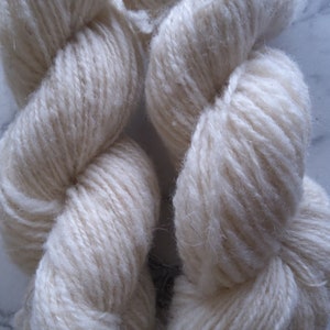 May include: Two skeins of white yarn, twisted together. The yarn is soft and fluffy, with a slightly textured surface.