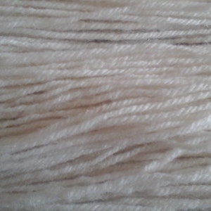 Könnte beinhalten: Nahaufnahme eines Knäuels cremefarbener Wolle. Die Garnstränge sind eng aneinander gepackt und bilden eine strukturierte Oberfläche. Das Garn wirkt weich und eignet sich für verschiedene Strick- oder Häkelprojekte.