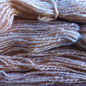 May include: A close-up of a pile of soft, pale pink yarn. The yarn is made of natural fibers and has a slightly fuzzy texture.