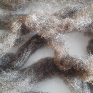 Puede incluir: Primer plano de un ovillo de hilo suave y esponjoso, gris y marrón. El hilo está enredado y anudado, creando un aspecto texturizado y orgánico.