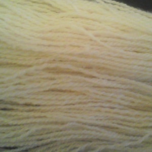 May include: A close-up of a skein of cream-colored yarn. The yarn is soft and fluffy, and it is perfect for knitting or crocheting.
