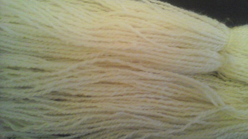 May include: A close-up of a skein of cream-colored yarn. The yarn is soft and fluffy, and it is perfect for knitting or crocheting.