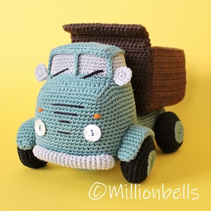 Può includere: Un camion ribaltabile giocattolo all'uncinetto nei toni del verde acqua, marrone, grigio e nero. Il camion presenta un design dettagliato con cabina, cassone e ruote. Il camion ha fari bianchi a bottone e un paraurti grigio. Lo sfondo è giallo pieno.