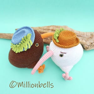 May include: Two crocheted kiwi bird plushies wearing hats. One kiwi is brown with a blue hat and green leaves. The other kiwi is white with an orange hat and green leaves.