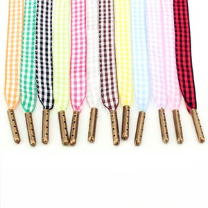 Peut inclure: Une collection de douze lacets en tissu avec un motif à carreaux vichy dans diverses couleurs dont orange, vert, noir, citron vert, rose, blanc, marron, jaune, bleu clair et rouge, chacun terminé par un embout en bronze métallique.