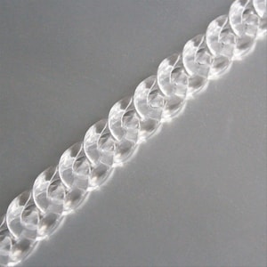 Puede incluir: Una cadena de plástico transparente con un diseño de eslabón curb. La cadena está hecha de eslabones individuales que están conectados entre sí para formar una cadena continua.