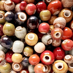 May include: Assortment of ceramic beads in various colors and patterns, including brown, red, green, and blue. The beads have a smooth, glazed finish and a hole in the center for stringing.