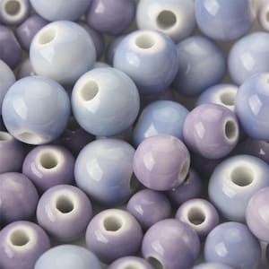 May include: A collection of ceramic beads in shades of light blue and lavender. The beads are round and have a hole in the centre for stringing.