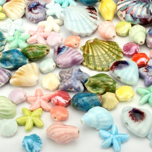 Könnte beinhalten: Eine Sammlung bunter Keramikperlen in verschiedenen Formen, darunter Muscheln und Seesterne. Die Perlen sind in Blau-, Grün-, Rosa-, Gelb- und Lilatönen gehalten. Diese dekorativen Perlen eignen sich ideal für Schmuckherstellung und Bastelprojekte.