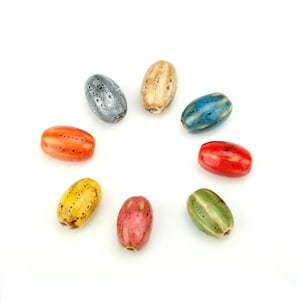 May include: Eight oval-shaped ceramic beads arranged in a circular pattern. The beads feature a glossy finish with varied speckled and streaked colour patterns in shades of blue, tan, orange, red, green, yellow, and pink, each with a central hole.