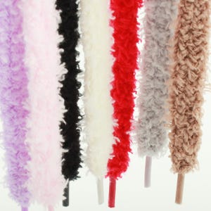 May include: A collection of seven fuzzy, textured shoelaces hanging vertically. The laces are colored in shades of light purple, pale pink, black, cream, bright red, light gray, and tan, each featuring a smooth, solid-colored plastic aglet tip.