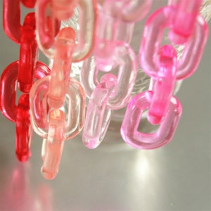 以下が含まれることがあります： ピンク、赤、透明のプラスチック製のリンクでできたチェーン。リンクはつながって連続したチェーンを形成しています。