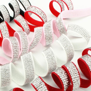 May include: A collection of coiled elastic ribbons featuring a sparkling silver glitter finish on one side and solid colored backing in black, red, pink, and white. These flexible bands are arranged in overlapping spirals, showcasing the contrast between the metallic silver texture and the smooth, matte fabric underside of each individual ribbon.