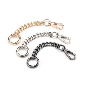 Peut inclure: Trois chaînes de sac à main en métal doré, argenté et noir. Chaque chaîne est dotée d'un mousqueton à une extrémité et d'un anneau circulaire à l'autre. Accessoire pour sacs à main.
