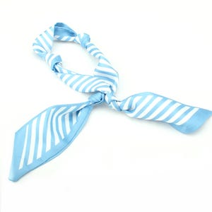 May include: A light blue and white striped neck scarf or hair ribbon featuring a smooth, satin-like texture. The fabric is tied into a decorative knot, creating two long, pointed ends and a looped section, showcasing a consistent diagonal pattern.