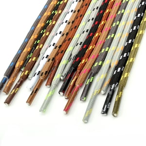 Puede incluir: Una colección de múltiples cordones redondos dispuestos en una fila paralela. Los cordones presentan varios colores, incluyendo negro, blanco, marrón, gris y oliva, con muchos incorporando patrones moteados contrastantes en su textura tejida.