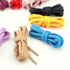 Puede incluir: Una colección de cordones planos y tejidos dispuestos en un patrón circular. El conjunto incluye paquetes individuales en rojo, rosa claro, negro, amarillo, azul brillante, beige y morado, cada uno con herretes de plástico a juego.