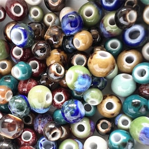 Puede incluir: Una colección de cuentas de cerámica en varios colores y patrones, incluyendo azul, verde, marrón y blanco. Las cuentas tienen un acabado liso y brillante y son perfectas para la elaboración de joyas o manualidades.