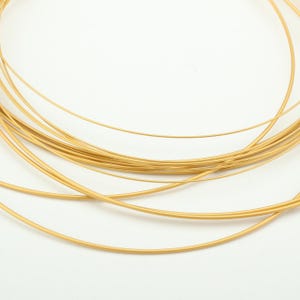 Puede incluir: Primer plano de un conjunto de alambre fino de color dorado. El alambre está enrollado y parece ser metálico. El fondo blanco liso resalta el color y la textura del alambre. El alambre probablemente se utiliza para la fabricación de joyas o manualidades.