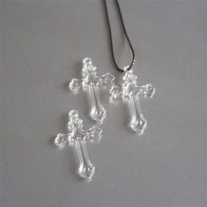 Peut inclure: Trois pendentifs en forme de croix en verre transparent, dont un sur une chaîne noire. Les croix ont un design détaillé et orné.
