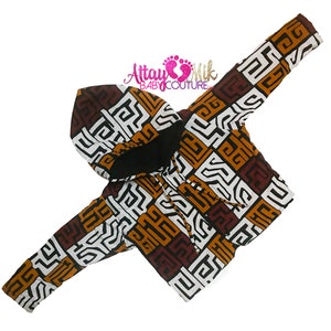 Op de afbeelding: Een hoodie met een geometrisch patroon in bruin, wit en oranje. De jas heeft een zwarte binnenkant en een trekkoord. De merknaam "Attay Mik BABY COUTURE" is zichtbaar op de afbeelding.