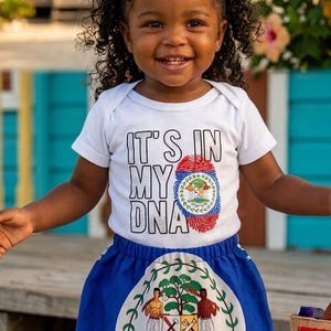 May include: A white short-sleeved bodysuit with the text IT'S IN MY DNA and a fingerprint graphic featuring the Belize flag, paired with a blue skirt displaying the Belize coat of arms and two red and blue hair bows.