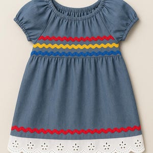 May include: Blue denim dress with short sleeves and a round neckline. The dress features a colorful wavy trim in red, yellow, and blue across the chest and a red trim at the hem. The hemline has a white, scalloped edge with floral cutouts.