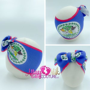 May include: A blue headband with a red trim and a bow, featuring the Belize coat of arms. The headband is displayed on a white mannequin head. The bow has a matching pattern.