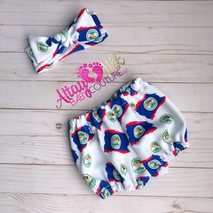 Può includere: Un completo per neonati bianco con fascia e bloomers, entrambi decorati con un motivo a bandiera del Belize. Il design della bandiera include colori blu, rosso e bianco, con l'emblema al centro. Il set è per bambini.