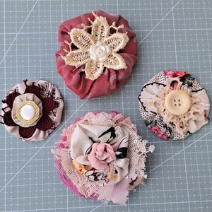 May include: A set of three ceramic mugs with a speckled, cream-colored glaze. Each mug features a different hand-painted floral design in shades of blue, green, and yellow. The mugs have a simple, rounded shape and a comfortable handle.