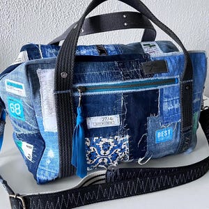 May include: A patchwork denim duffel bag with a black shoulder strap and handles. The bag features various denim patches, including a blue and white patterned square, and the word "BEST" on a blue label. A blue tassel hangs from the zipper.